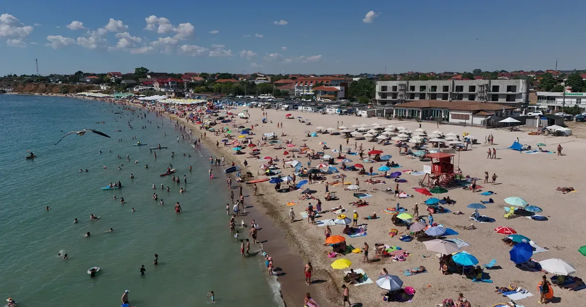 Plajă aglomerată pe litoralul românesc, cu umbrele colorate și turiști.