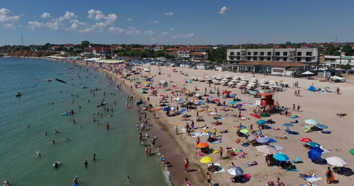Plajă aglomerată pe litoralul românesc, cu umbrele colorate și turiști.