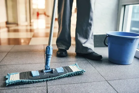 Persoană care curăță podeaua cu mopul într-un spațiu interior.