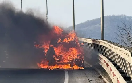 Un autoturism în flăcări pe marginea drumului, fum gros în jur.