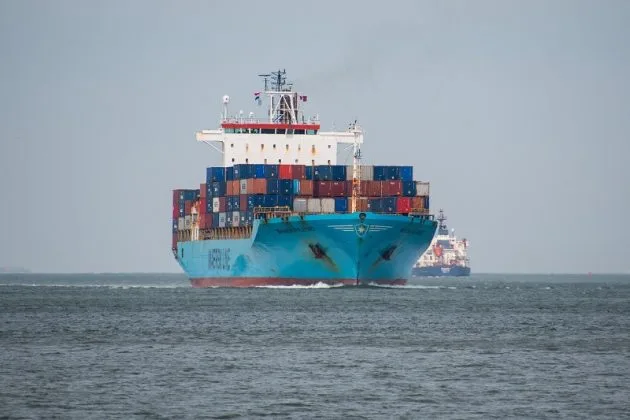 Nava cargo navigând pe apă, încărcată cu containere colorate.