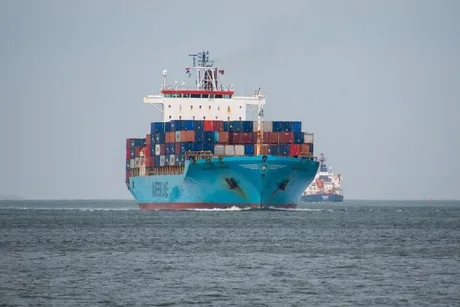Nava cargo navigând pe apă, încărcată cu containere colorate.