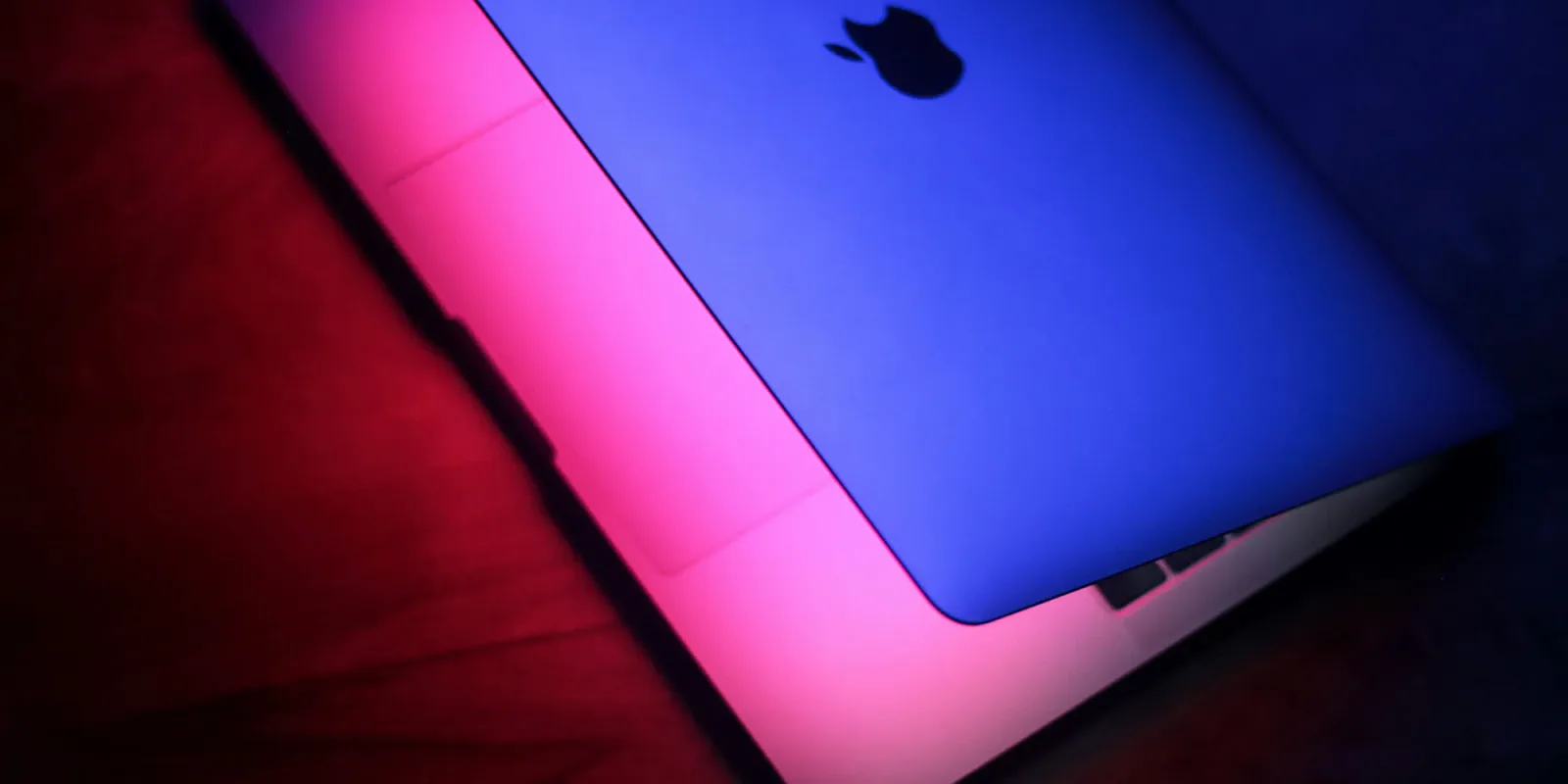Laptop Apple cu iluminare colorată pe fundal întunecat.