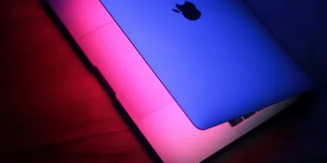 Laptop Apple cu iluminare colorată pe fundal întunecat.