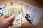 Bancnote românești în mână, documente pe masă.