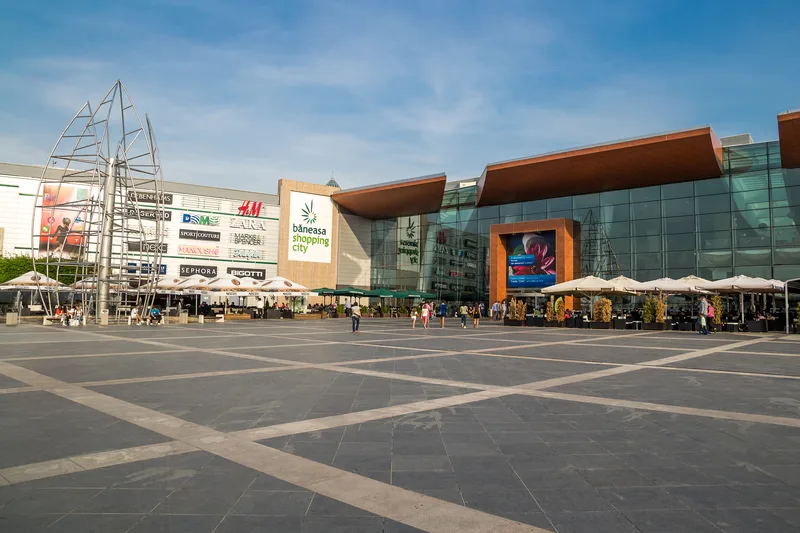 O imagine a unui mall modern din București, cu magazine și terase pline de oameni.
