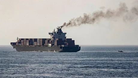 Nava cargo navigând pe mare, emanând fum de la motoare.