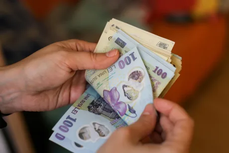 Bancnote românești în mâini, simbolizând puterea de cumpărare scăzută.