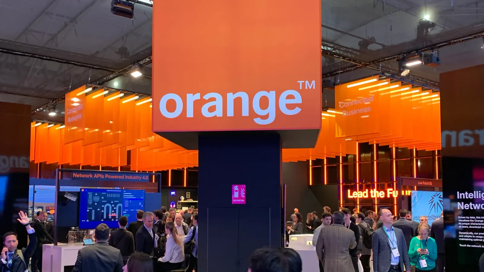 Stand Orange la un eveniment, cu oameni discutând și tehnologie expusă.
