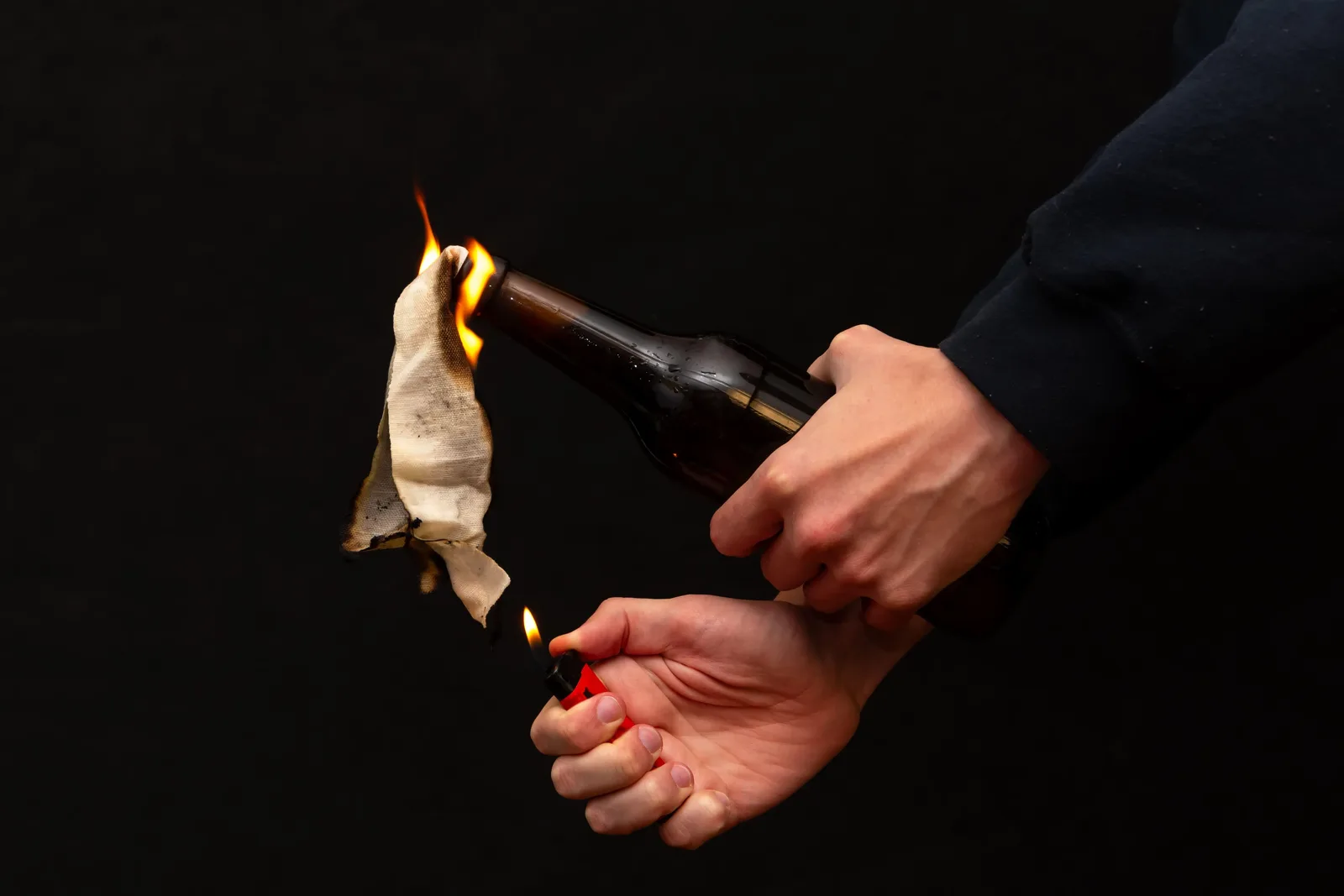 O mână ține un cocktail Molotov aprins, pregătit pentru a fi aruncat.