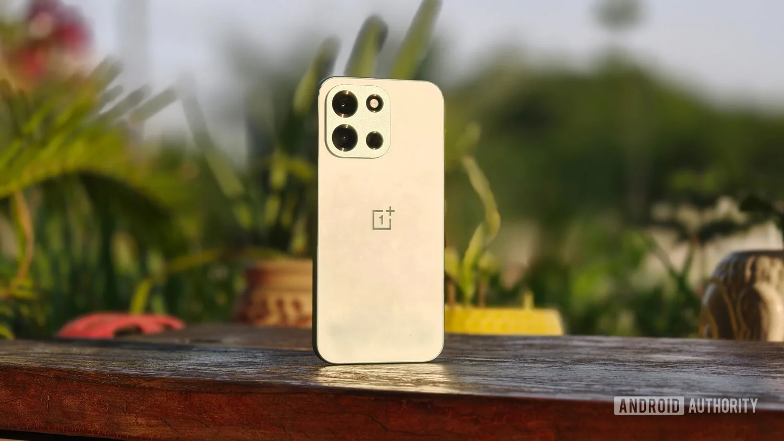 Un telefon OnePlus pe o masă, înconjurat de plante verzi.