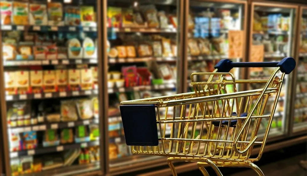Carucior de cumpărături în fața rafturilor cu produse alimentare.