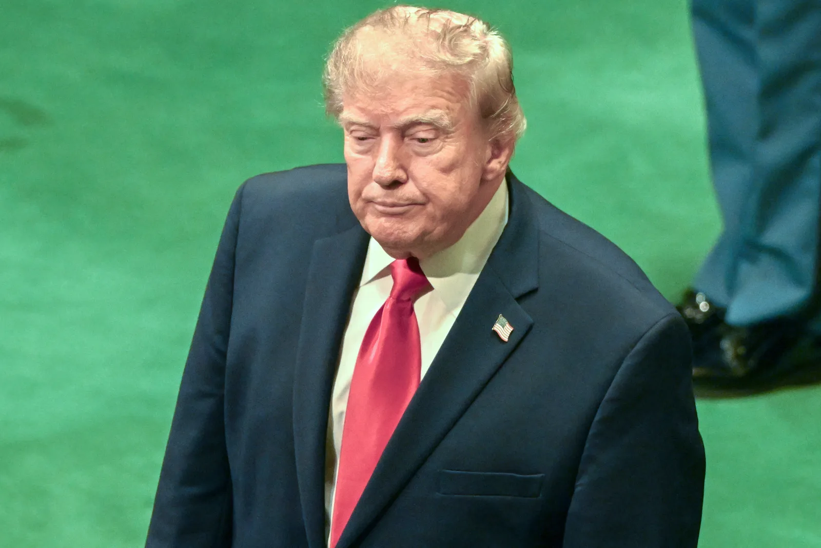 Donald Trump pe fundal verde, cu o expresie serioasă, în timpul unei conferințe.