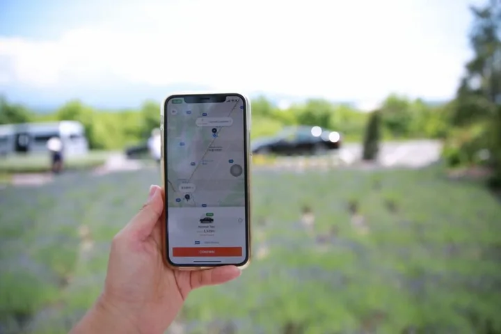 Un telefon mobil afișează o aplicație de ride-hailing în aer liber, cu peisaj verde în fundal.