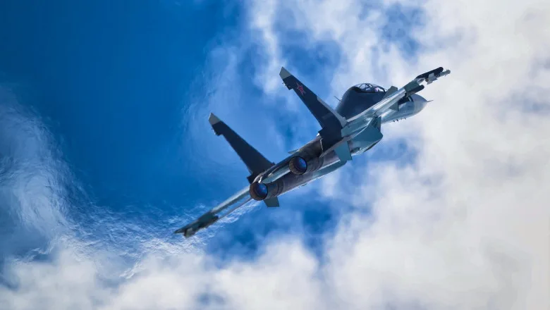 Avion de vânătoare Su-30SM zburând pe un fundal de nori albi.