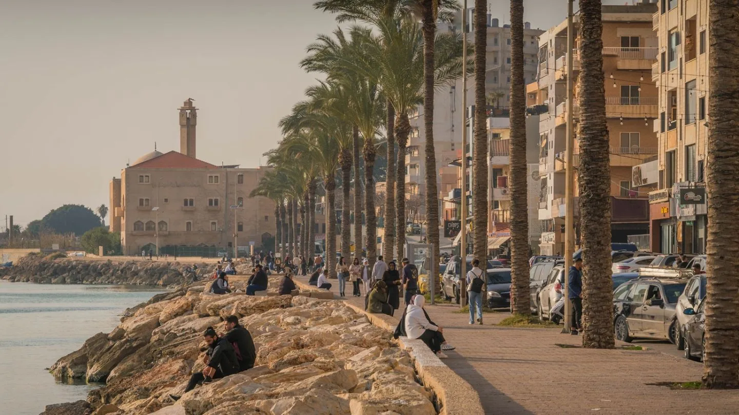 Peisaj urban din Liban, cu palmieri și oameni pe malul apei.