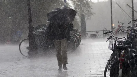 Persoană cu umbrelă în ploaie torențială pe stradă.
