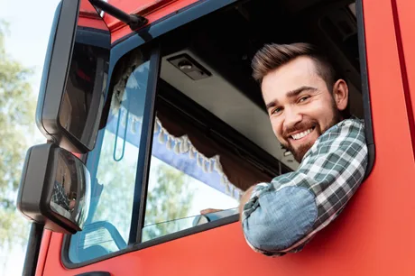 Șofer zâmbitor într-un camion roșu, reflectând optimismul în transport.