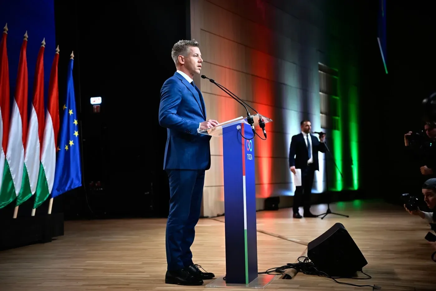 Péter Magyar vorbește la un eveniment oficial, cu steaguri în fundal.