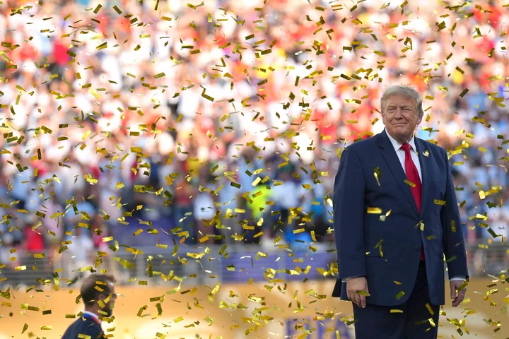 Donald Trump pe o scenă, înconjurat de confetti aurii, la un eveniment public.