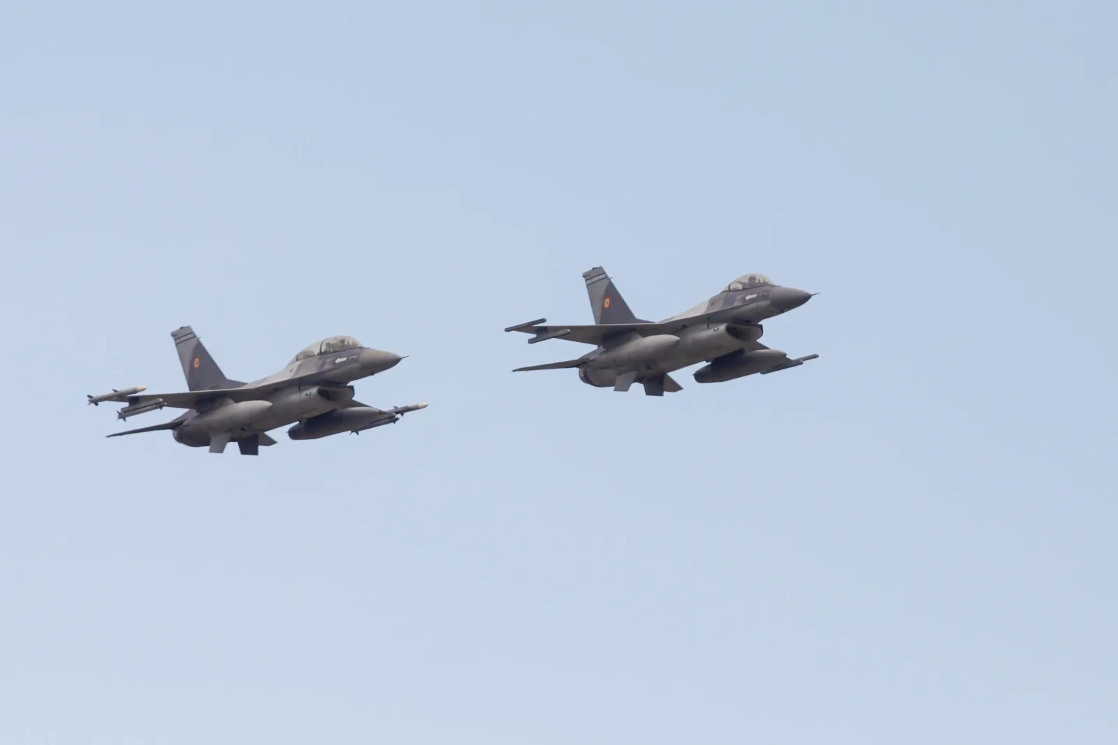 Două aeronave F-16 zburând în patrulare deasupra unei zone agricole.