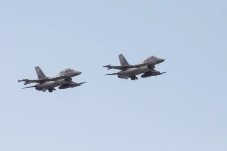 Două aeronave F-16 zburând în patrulare deasupra unei zone agricole.