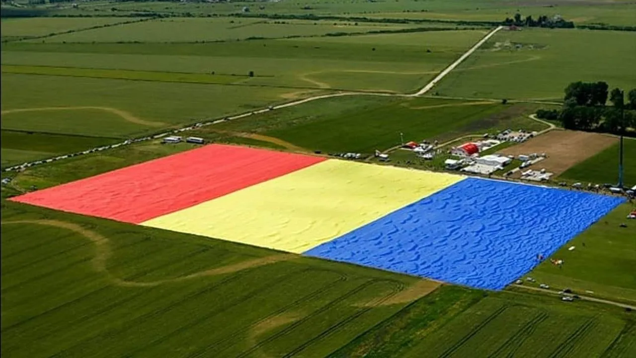 Steag uriaș al României desfășurat pe un câmp verde.