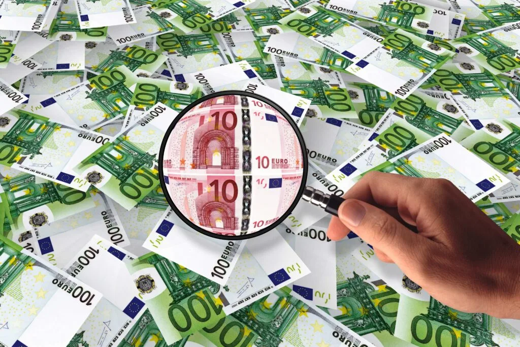Bancnote euro aranjate, cu o lupă focalizată pe o bancnotă de 10 euro.