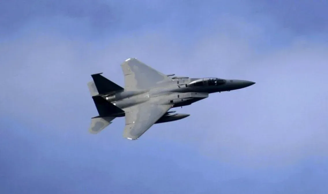 Avion militar F-15K în zbor, cu cer albastru în fundal.