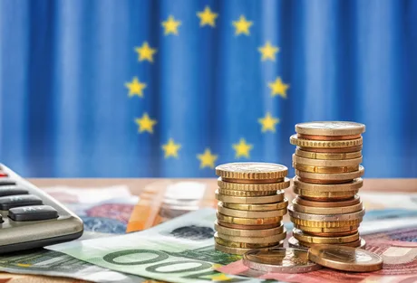 Monede și bancnote pe fundalul steagului Uniunii Europene.