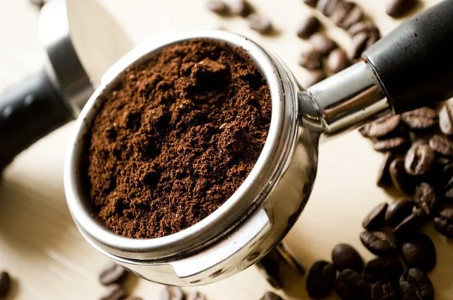 Cafea măcinată într-un portafiltru, alături de boabe de cafea.