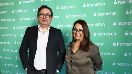Două persoane zâmbind, în fața unui fundal verde cu logo-ul HomeRun.