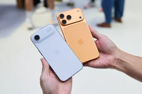 Două smartphone-uri Apple, unul alb și unul portocaliu, în mâinile unei persoane.