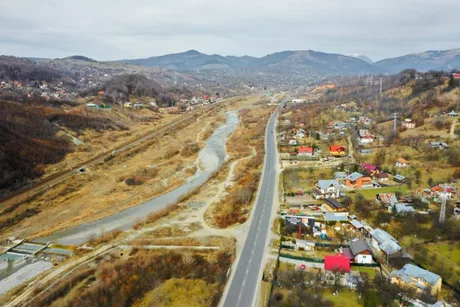 Peisaj montan cu drum și așezări în apropierea unei ape curgătoare.