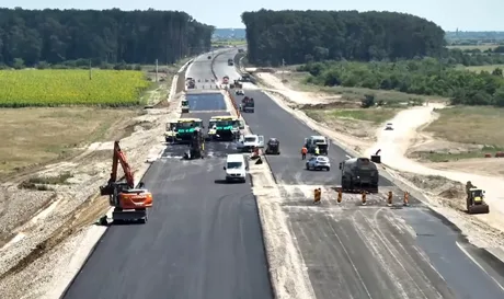 Lucrări de asfaltare pe lotul 1 al autostrăzii A0 Nord, cu utilaje și muncitori activi.