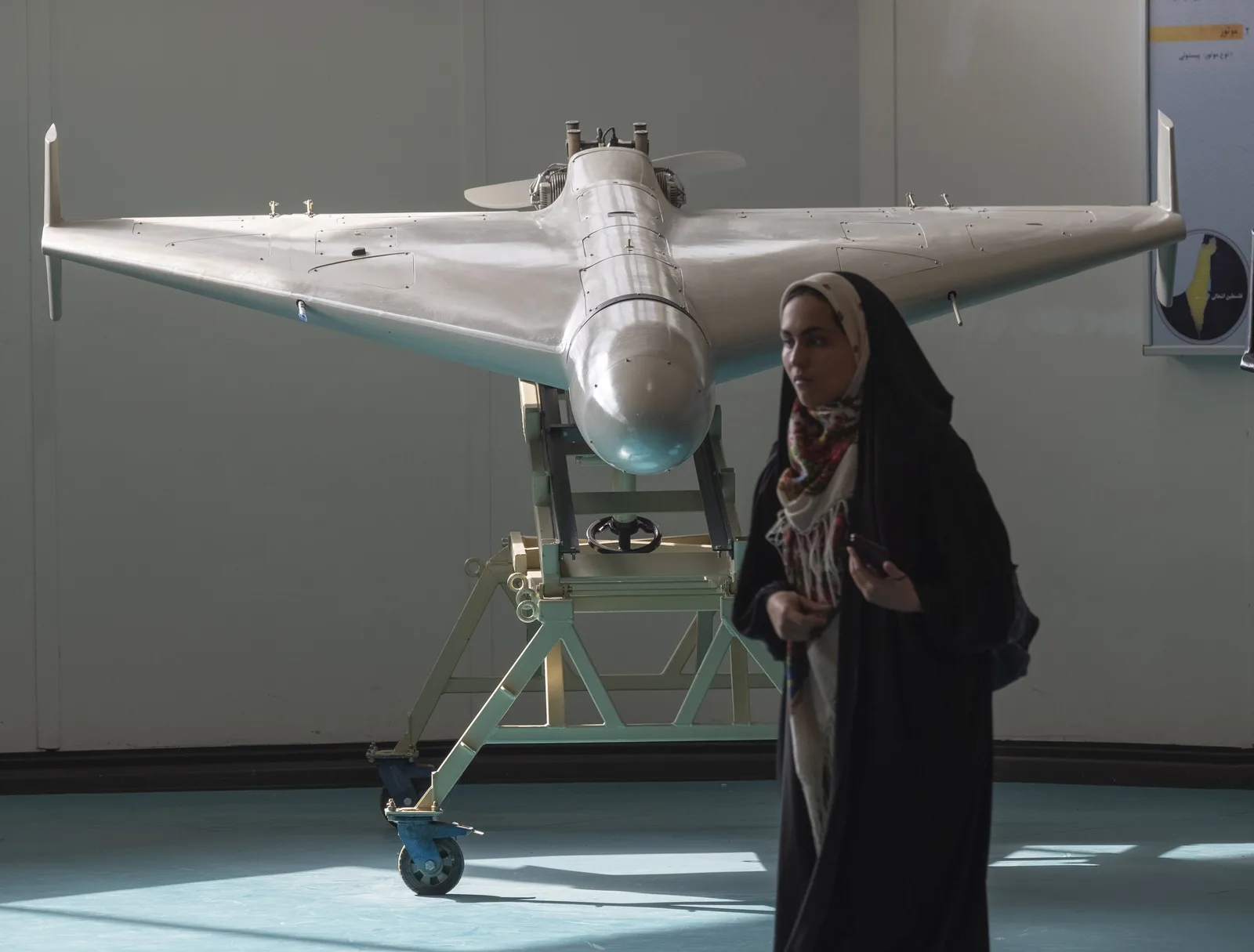 O dronă Shahed expusă, cu o femeie în fundal, într-un mediu industrial.
