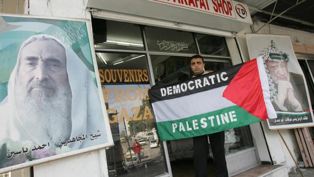 Un bărbat ținând un steag palestinian în fața unui magazin din Gaza.