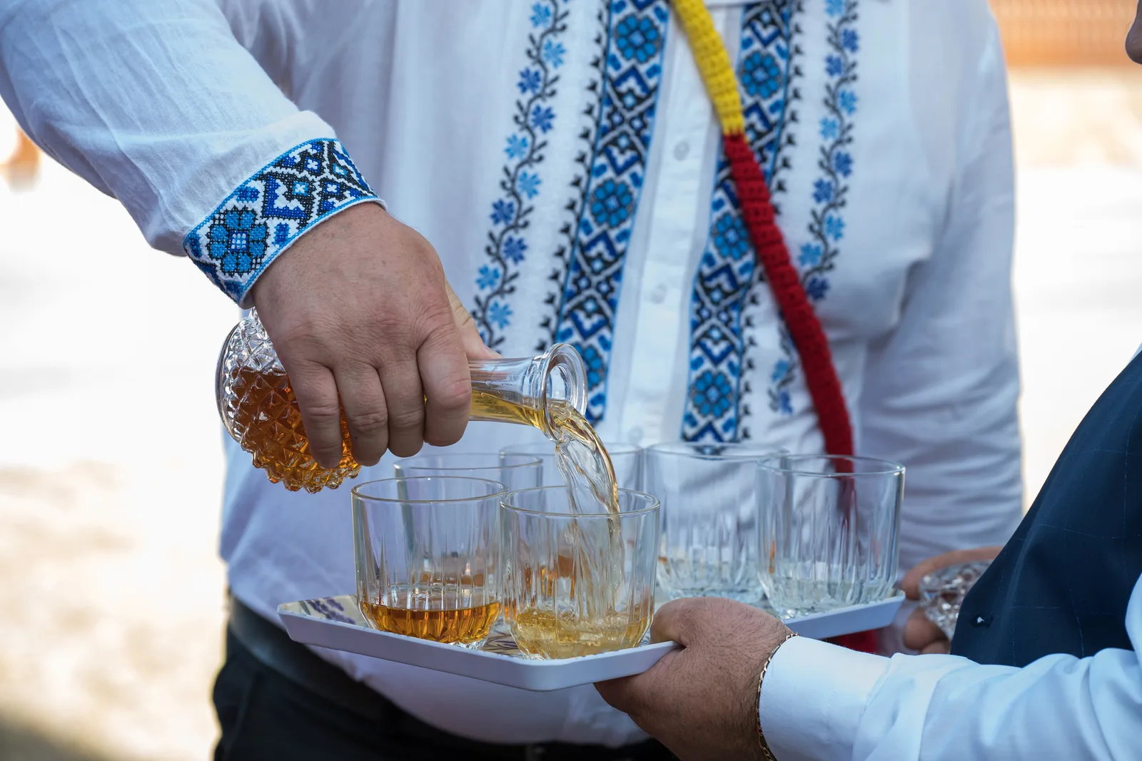 Un bărbat toarnă țuică dintr-o carafă în pahare.