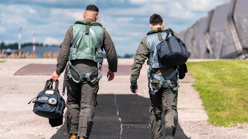 Doi piloți se îndreaptă spre aeronave, pregătiți pentru misiune.