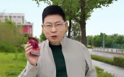Un bărbat ținând un telefon mobil în mână, zâmbind în aer liber.