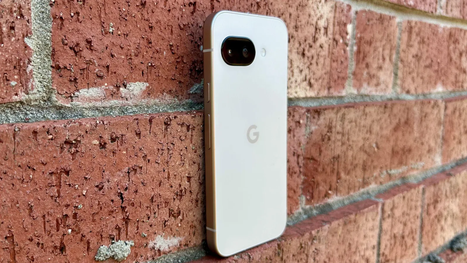 Un telefon Pixel 10a pe un zid de cărămidă, cu un design elegant.