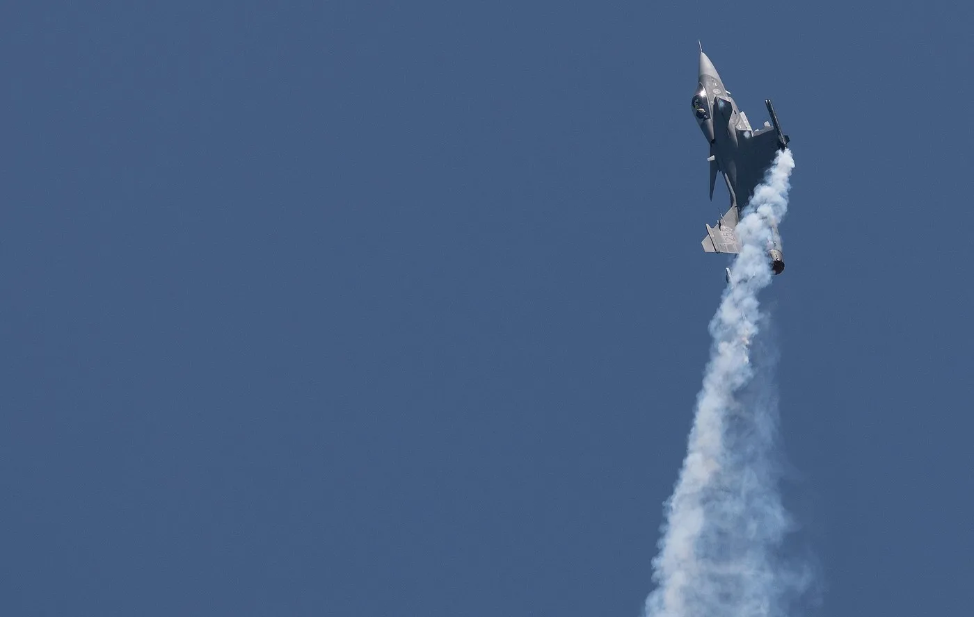 Avion militar Gripen în timpul unui zbor de antrenament, linii de fum în urma sa.
