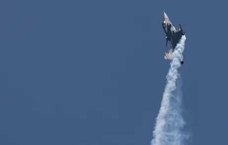 Avion militar Gripen în timpul unui zbor de antrenament, linii de fum în urma sa.