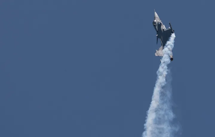 Avion militar Gripen în timpul unui zbor de antrenament, linii de fum în urma sa.