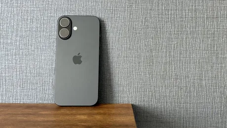 iPhone 16 pe o masă, cu un fundal texturat gri.