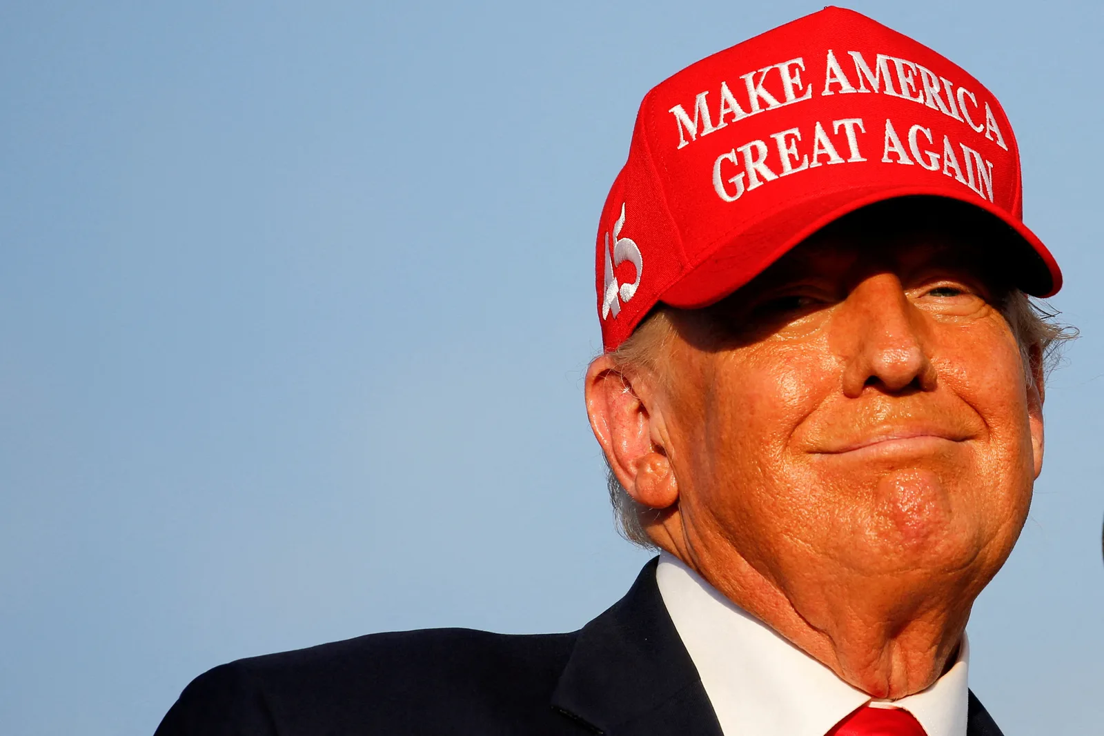Donald Trump zâmbind, purtând o șapcă roșie cu mesajul politic.