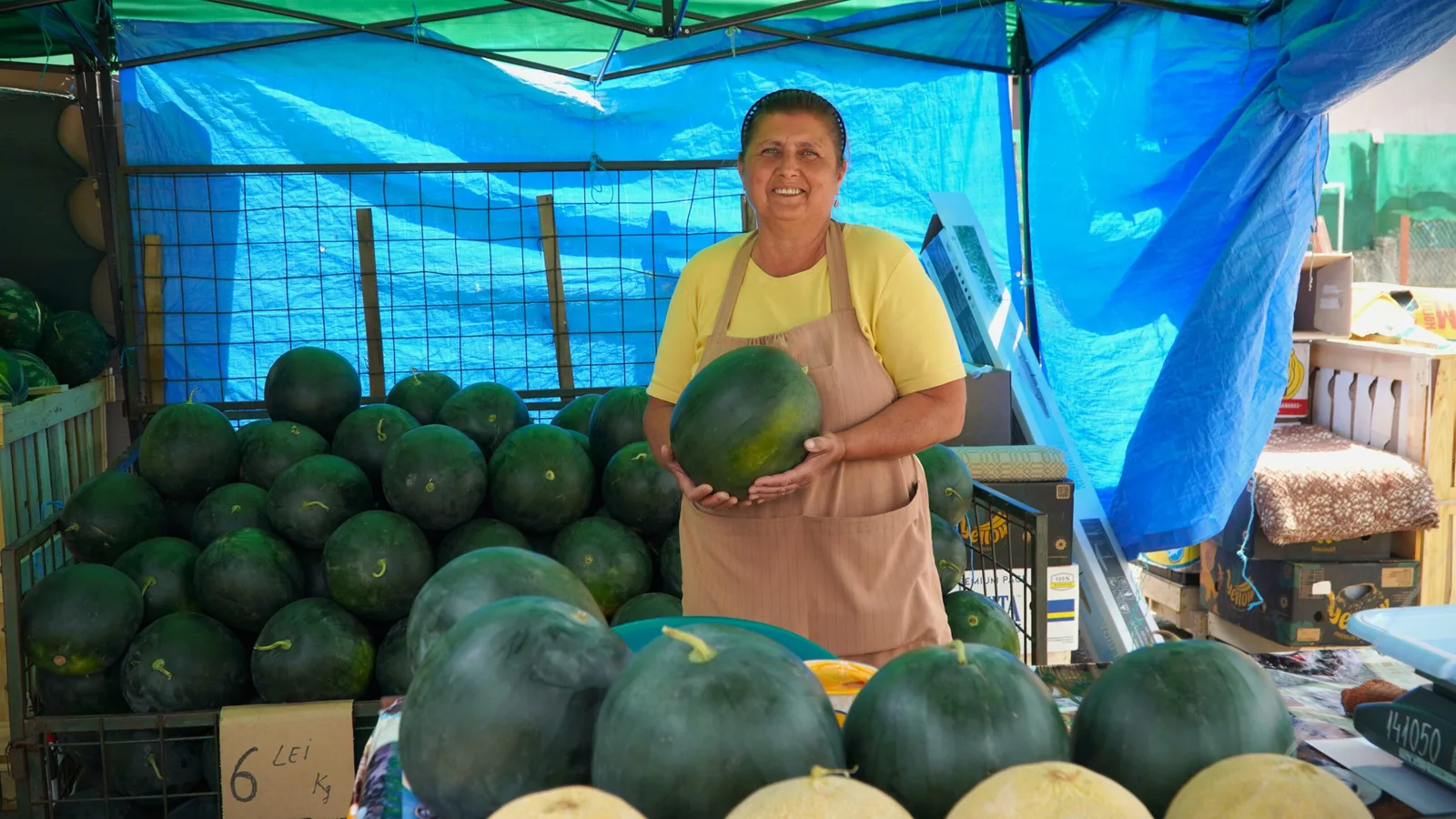 Fermieră zâmbitoare la tarabă, cu pepeni proaspeți în jur.