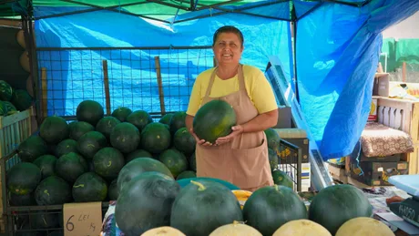 Fermieră zâmbitoare la tarabă, cu pepeni proaspeți în jur.