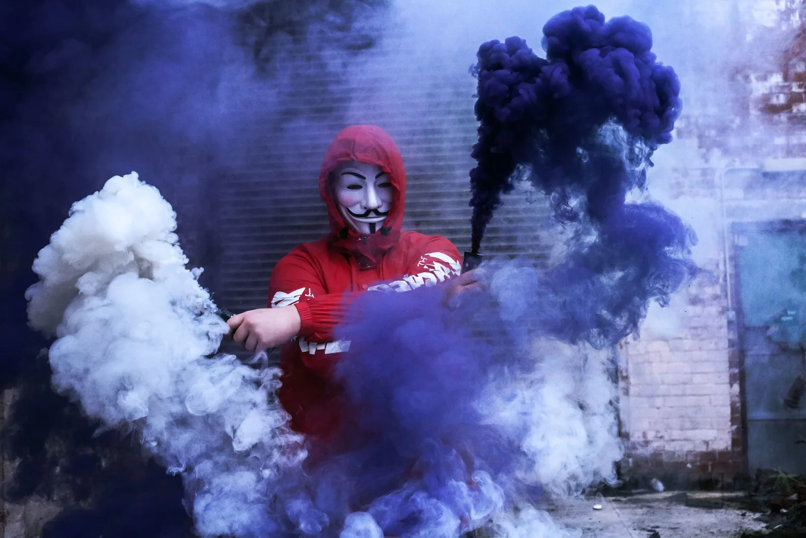 Persoană cu mască și fum colorat, simbolizând amenințări cibernetice.