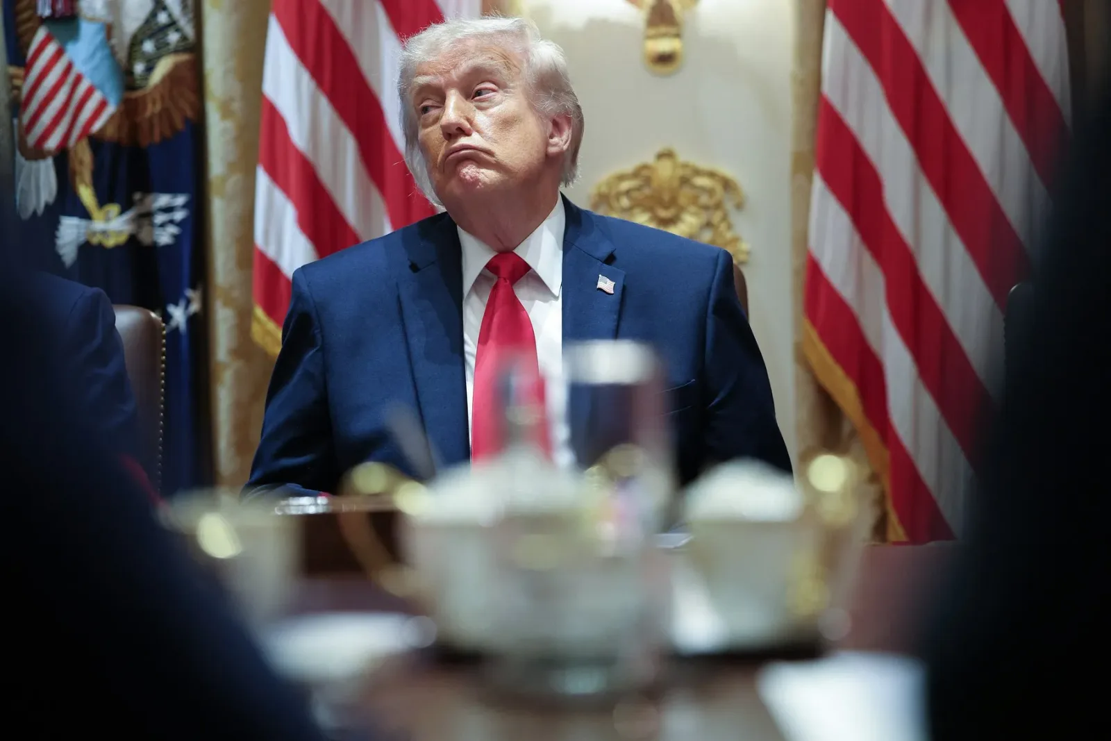 Donald Trump în timpul unei întâlniri oficiale, cu steagurile SUA în fundal.